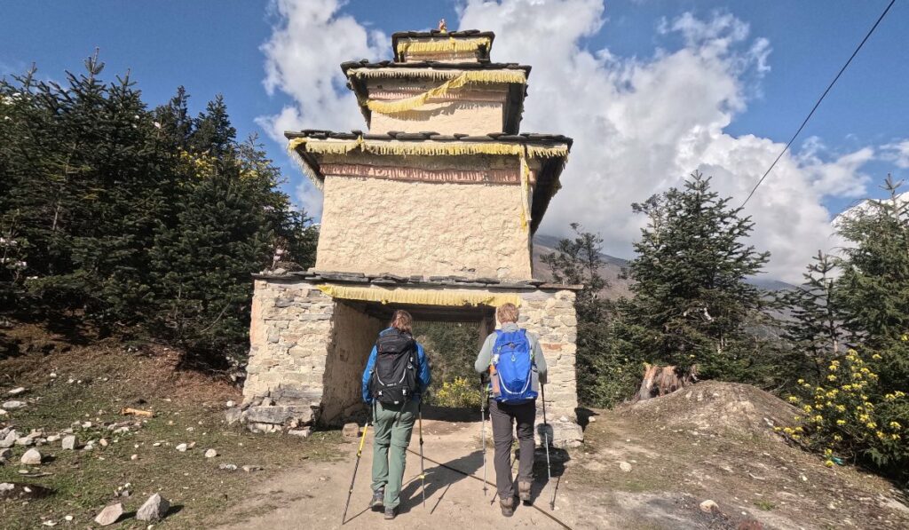 Trekkers walking through a traditional chorten gate on the Tsum Valley trail