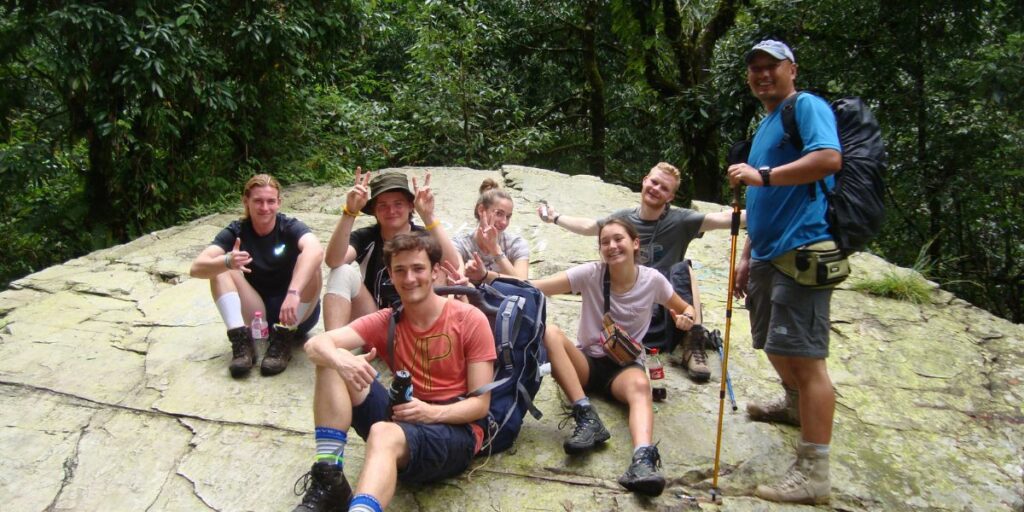 trekkers resting on rocky forest ledge during mountain trail in nepal