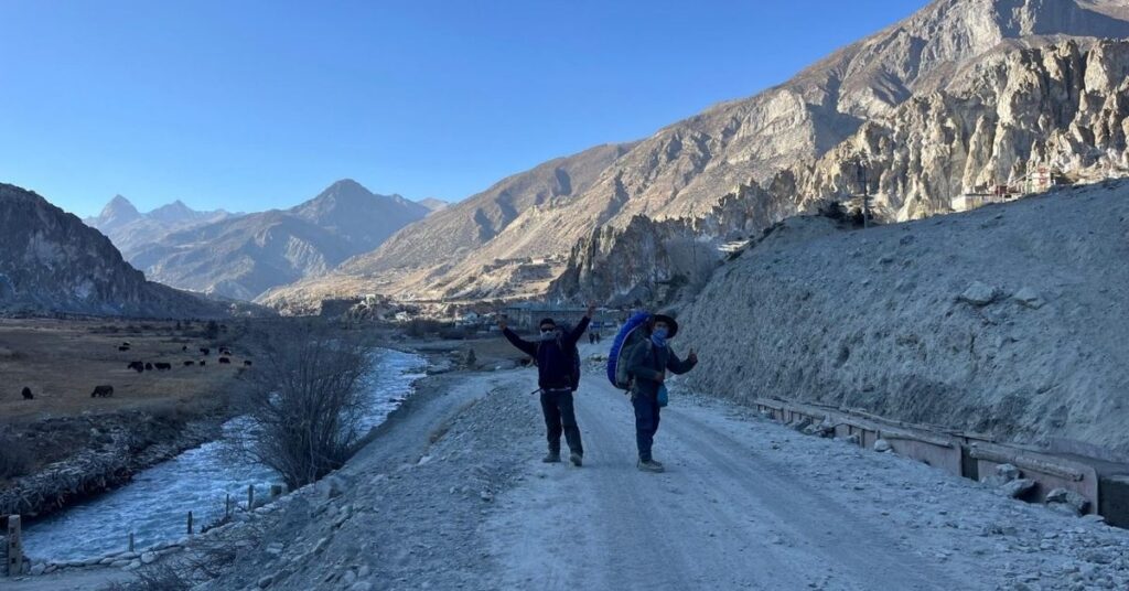 Trekkers joyfully walking beside a riverbank with yaks grazing in the Manang valley landscape