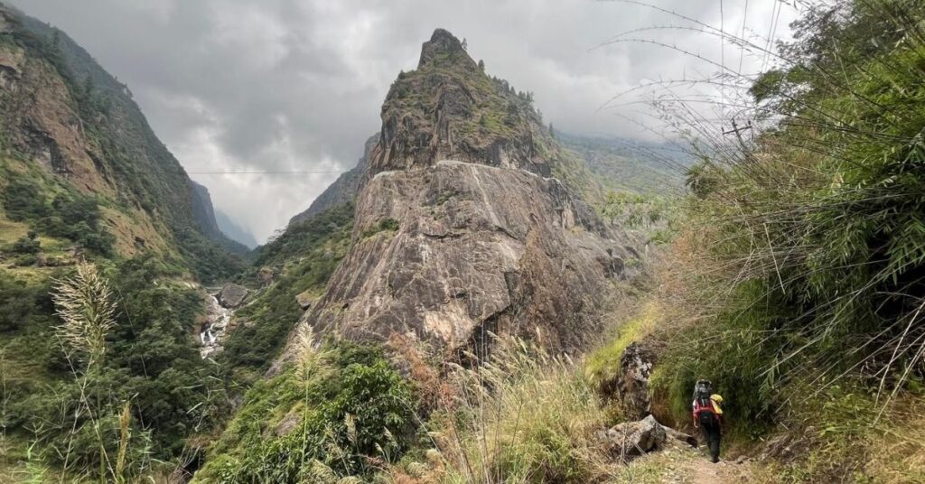 Walking through a lush green valley with towering cliffs on the route to Manang Village