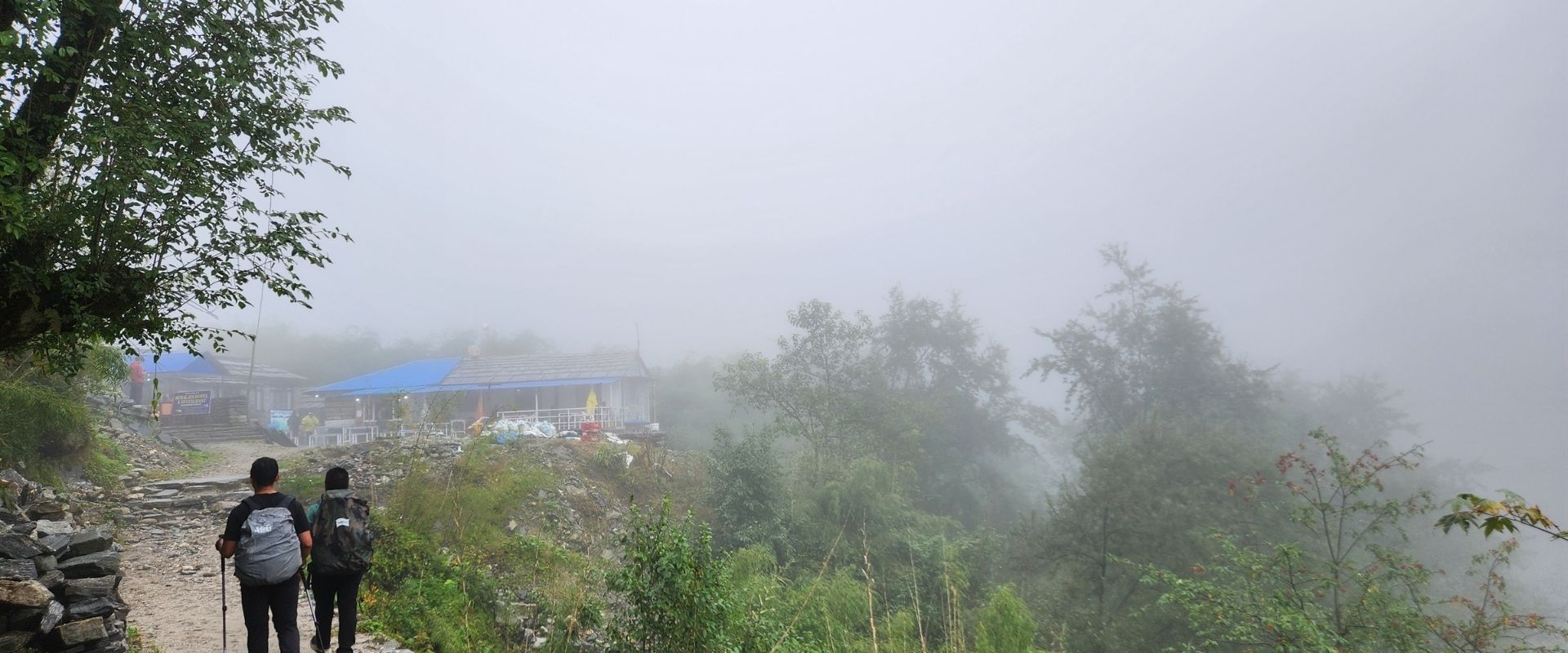 Beginner trekkers on the ABC trail walking towards teahouses in the foggy Himalayan landscape