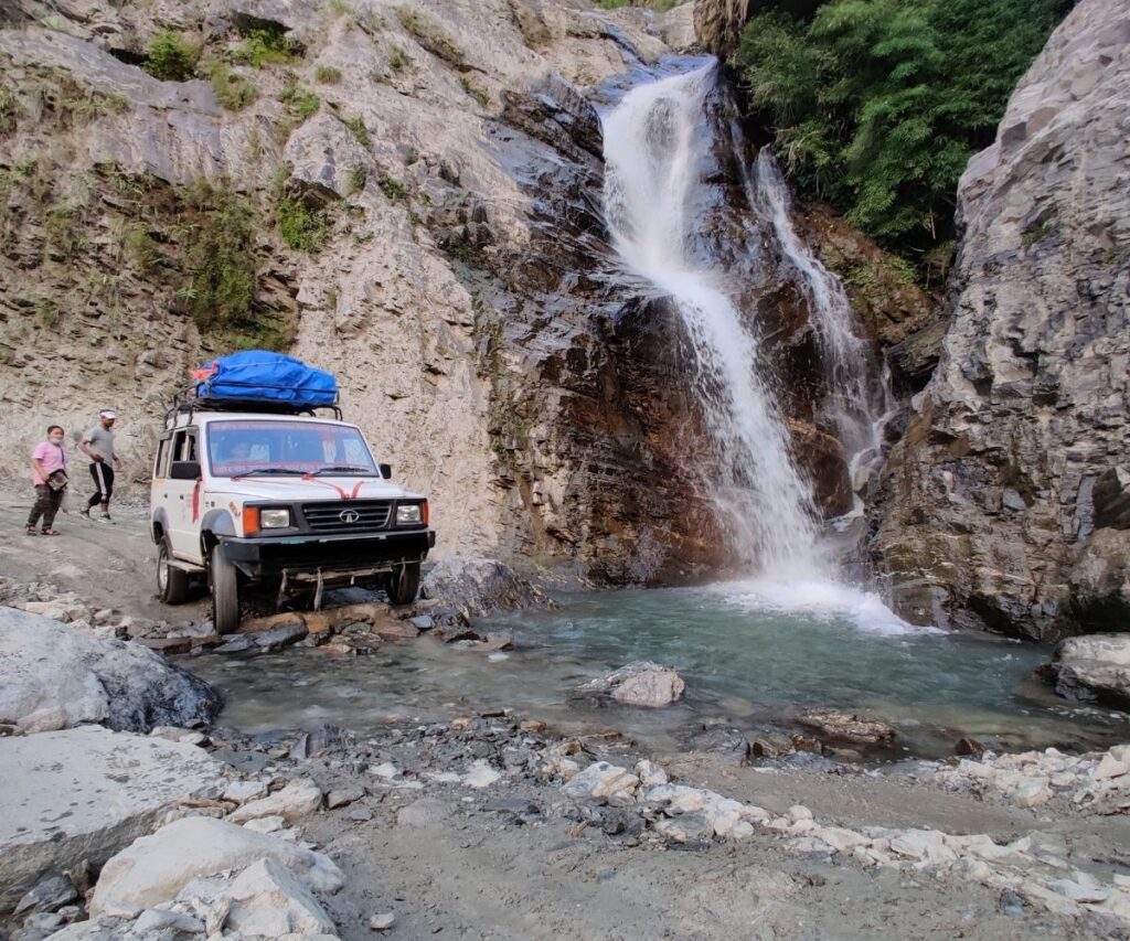 Jeep crossing rocky stream near waterfall on Manaslu Circuit Trek