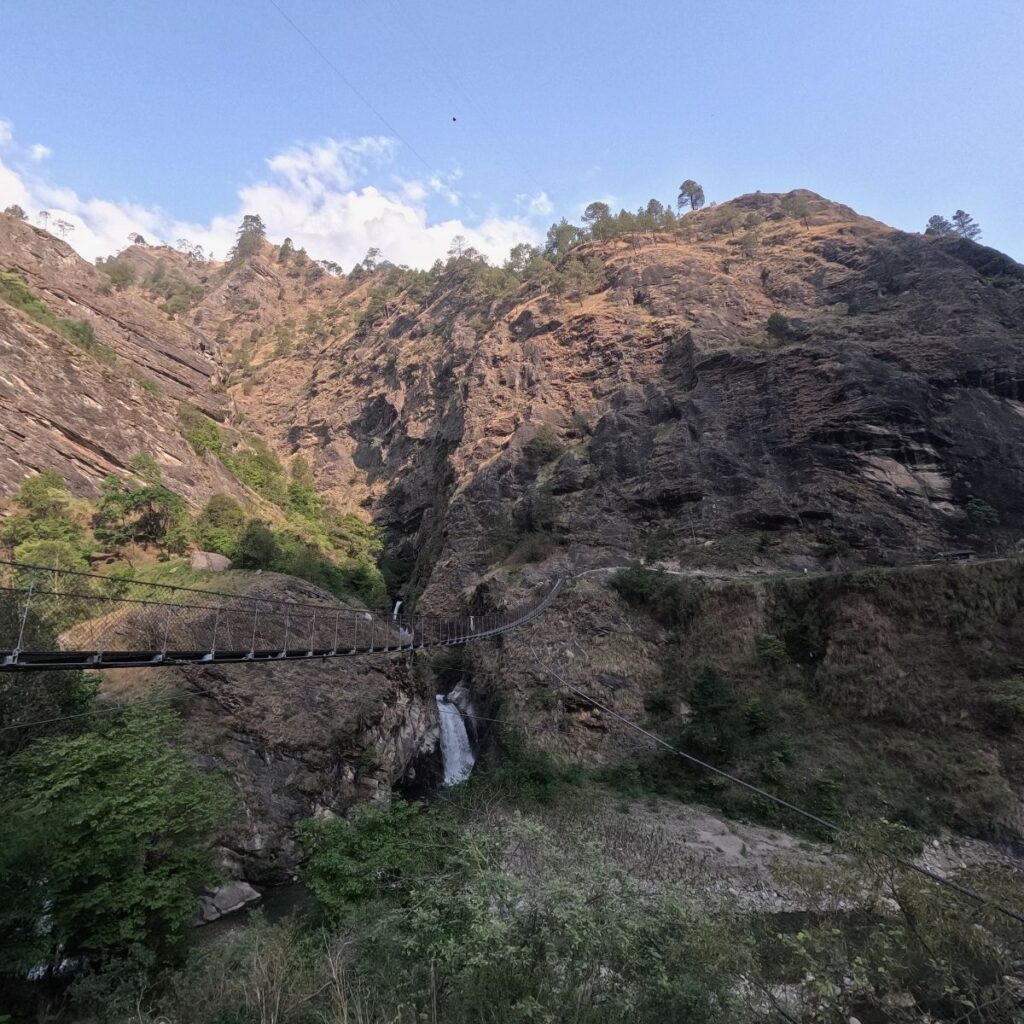 Suspension bridge crossing a deep gorge with waterfall views on the Tsum Valley trek