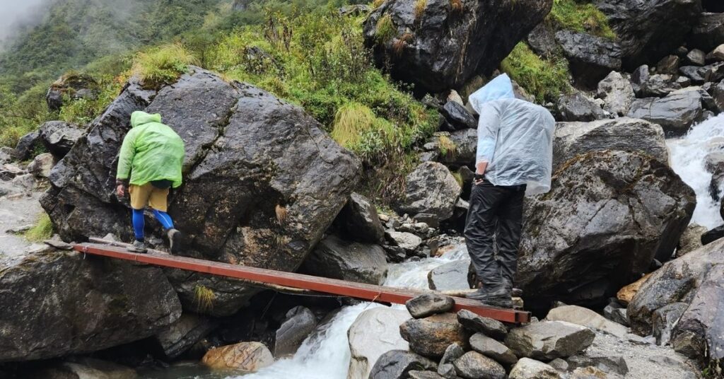 Trekkers on ABC journey carefully cross a narrow wooden bridge