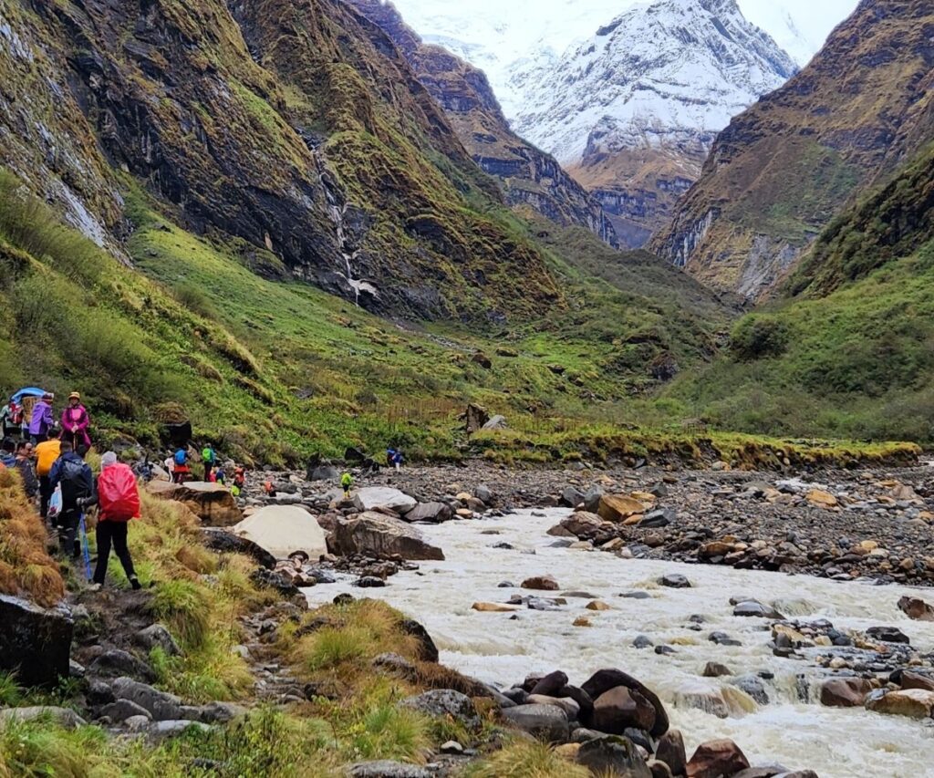Trekkers walking along a rocky trail beside a river in the Annapurna region