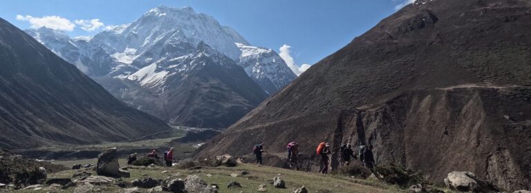 Trekkers walking beneath snow-covered peaks on a clear day in the Manaslu region