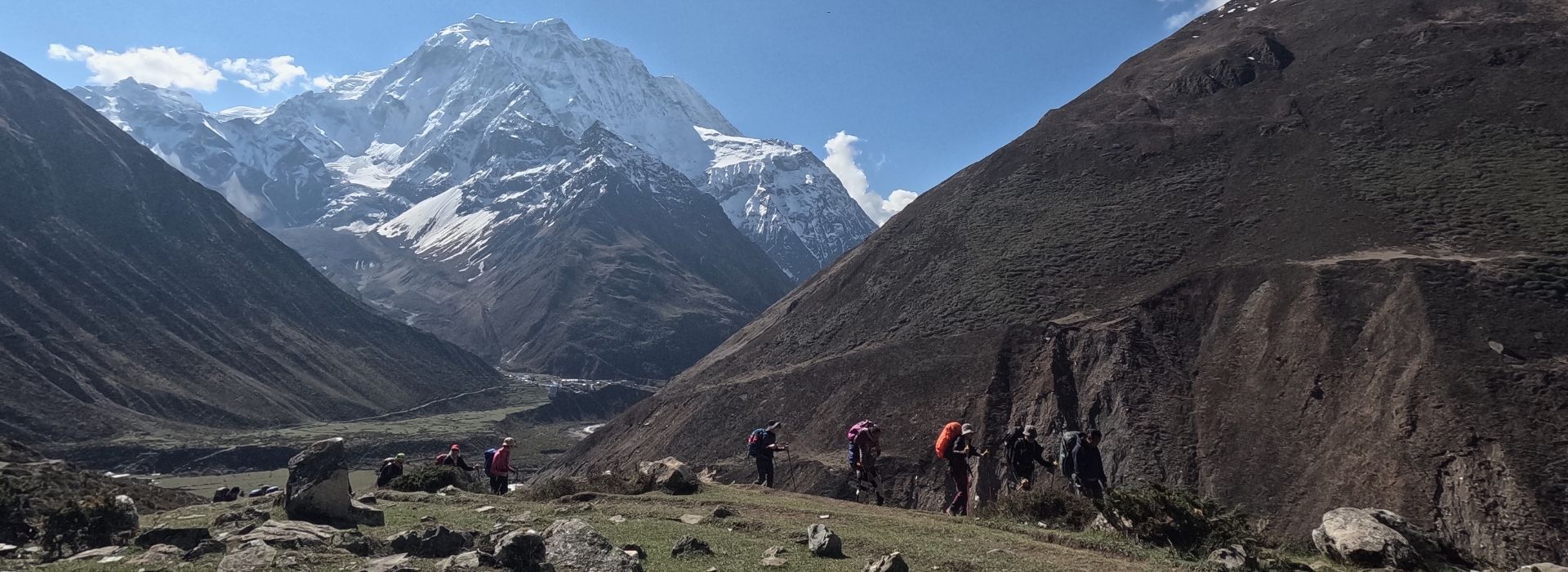 Trekkers walking beneath snow-covered peaks on a clear day in the Manaslu region