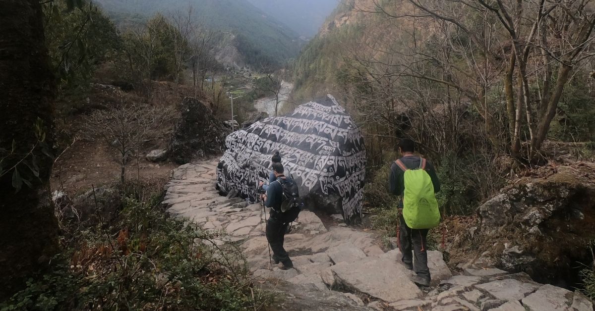 EBC trek with hikers in boots passing Buddhist carved rock