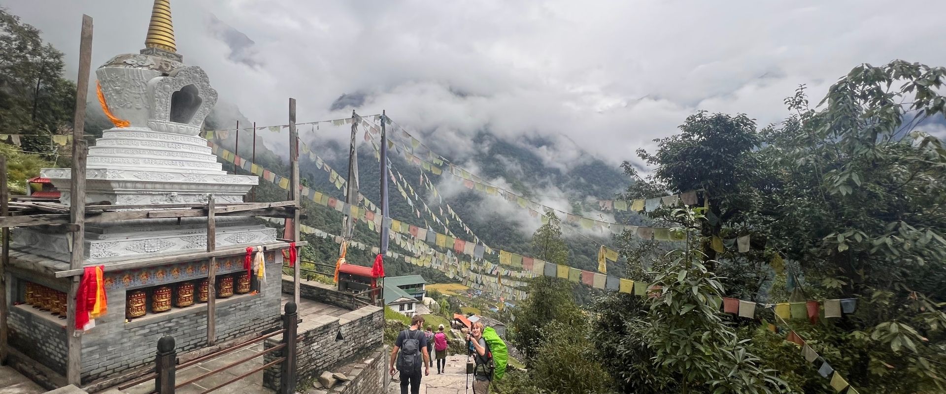 Hikers strolling through Chhomrong with village houses, stupa, and misty hills in the background