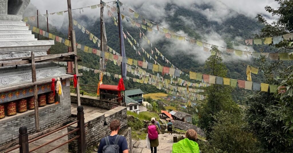 Trekkers walking past a stupa in Chhomrong village, surrounded by green hills and prayer flags
