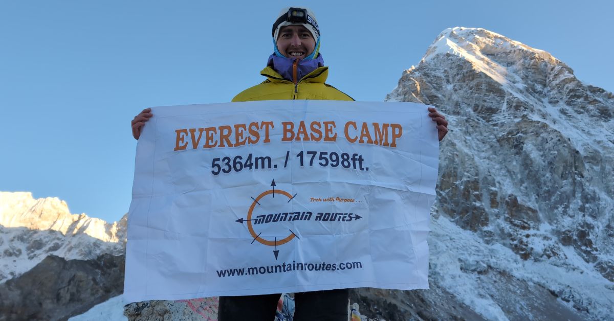 Trekker holding an Everest Base Camp 5364m banner after completing trek with Mountain Routes