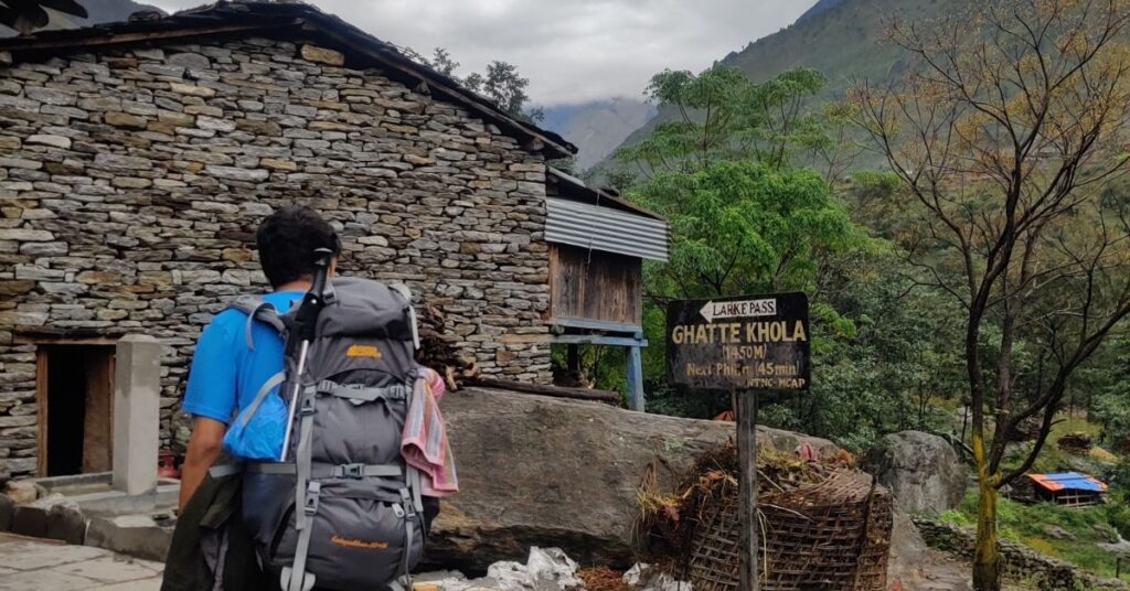 Backpacker passing stone houses near Ghatte Khola on Manaslu route