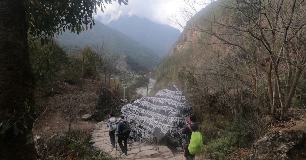 Trekkers walking past a large Mani stone
